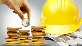 mano che impila monete con sullo sfondo un caschetto e dei guanti da lavoro